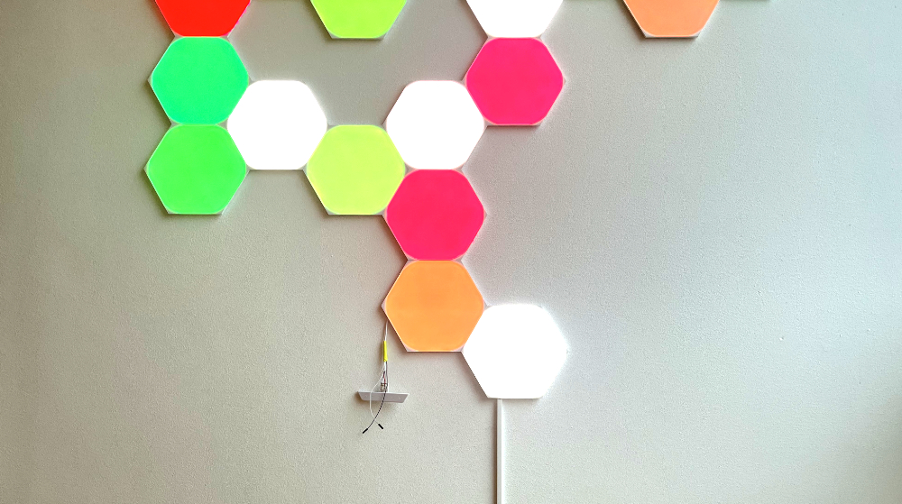 Nanoleaf Shapes panels, lit in various colours, on a white wall