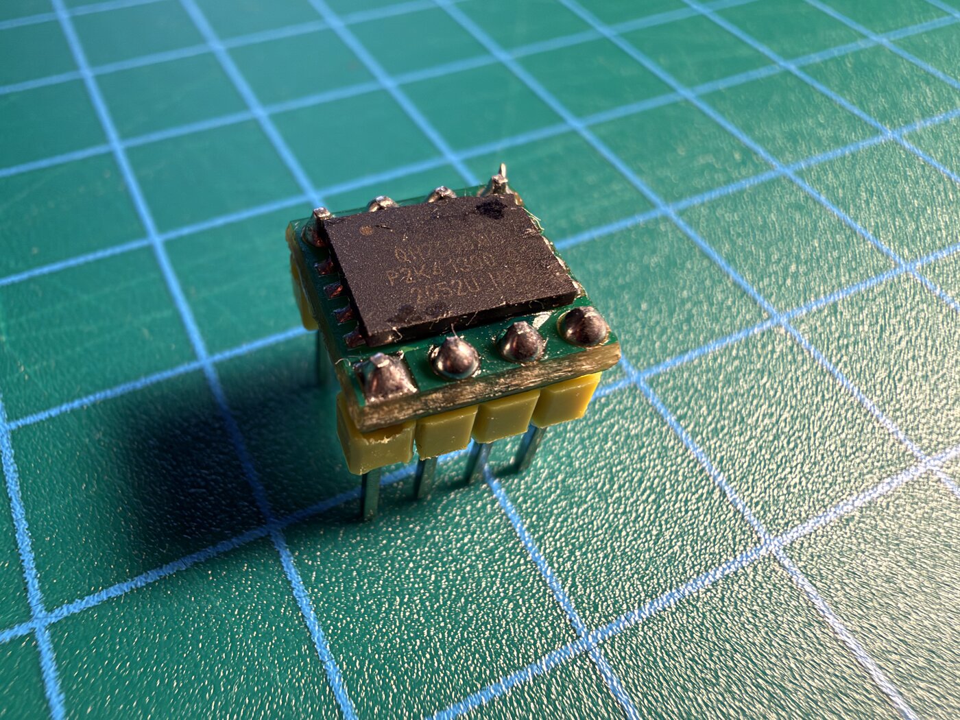 The SPI flash chip soldered onto a small WSON-to-DIP adapter board with header pins, standing on a cutting mat